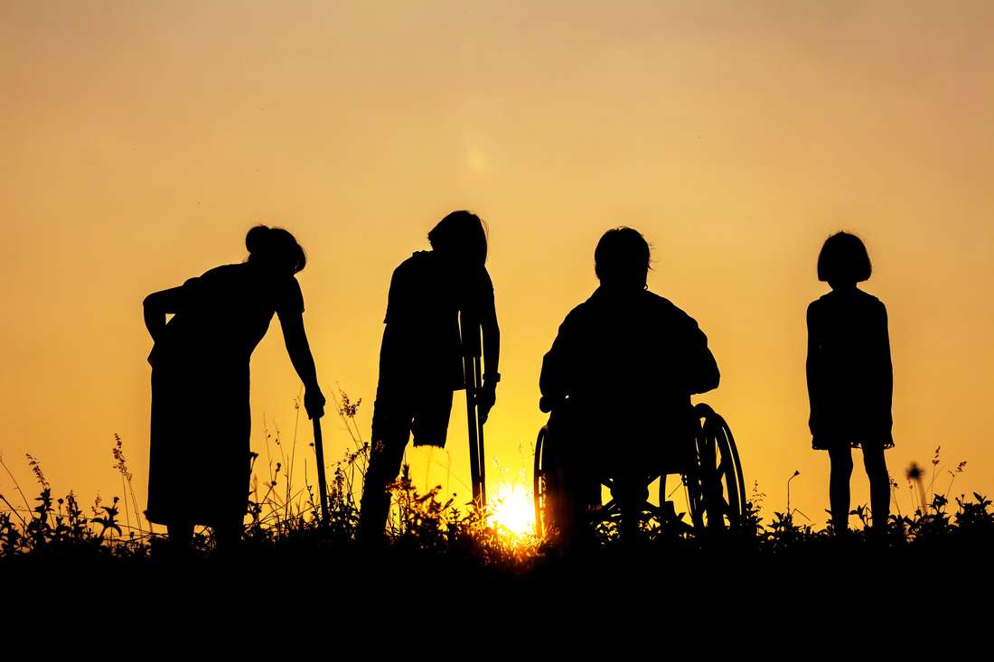 4 silhouettes of people watching the sunset on a hill. From left to right - Grandmother, leg amputee, Wheelchair, child